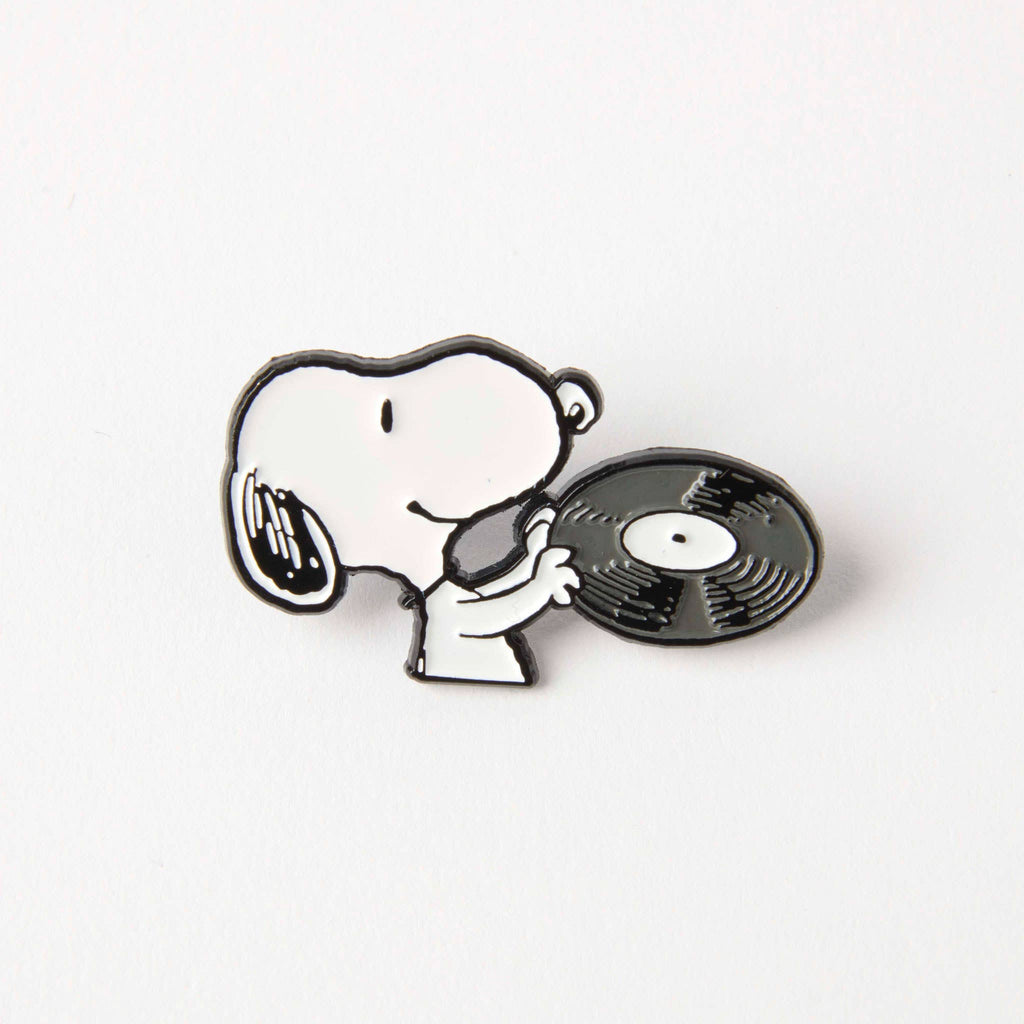 Enamel pin of Snoopy holding a vinyl record, ideal for music enthusiasts and Peanuts fans.