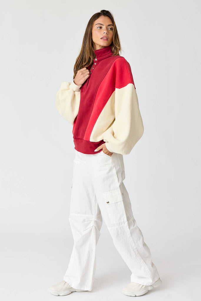 Woman wearing an oversized washed colorblock sweater in red and cream with white pants. 