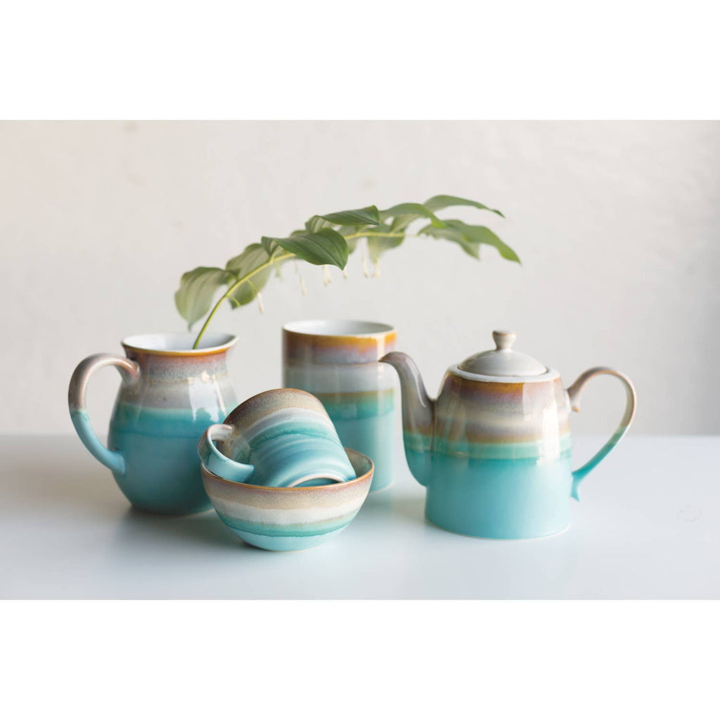 Ceramic mug with an ombre design in earthy brown and aqua tones, featuring a round handle.
