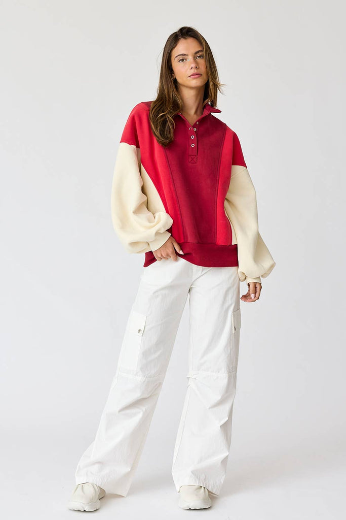 Woman wearing an oversized washed colorblock sweater in red and cream with white pants. 