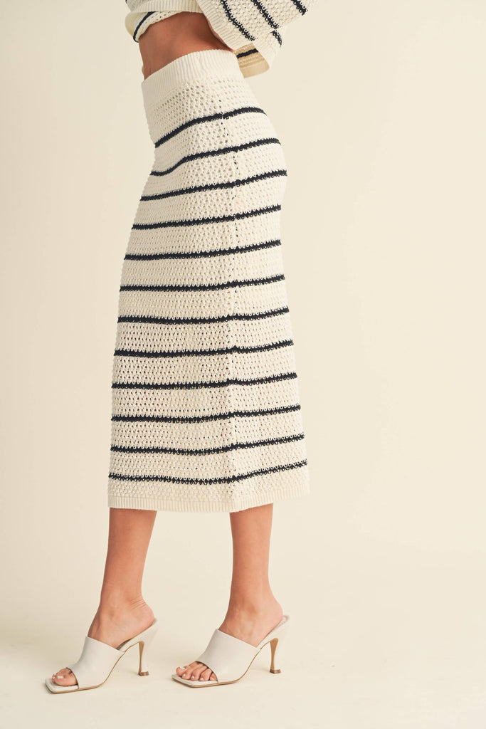 Woman wearing a high-waisted, ivory and black striped knit midi skirt with slide sandals.
