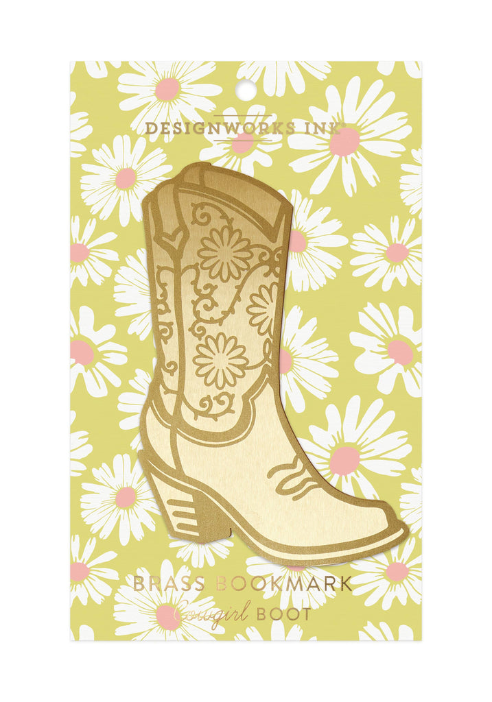 A brass bookmark shaped like a cowgirl boot with floral engravings, displayed on a daisy-patterned yellow backing card.