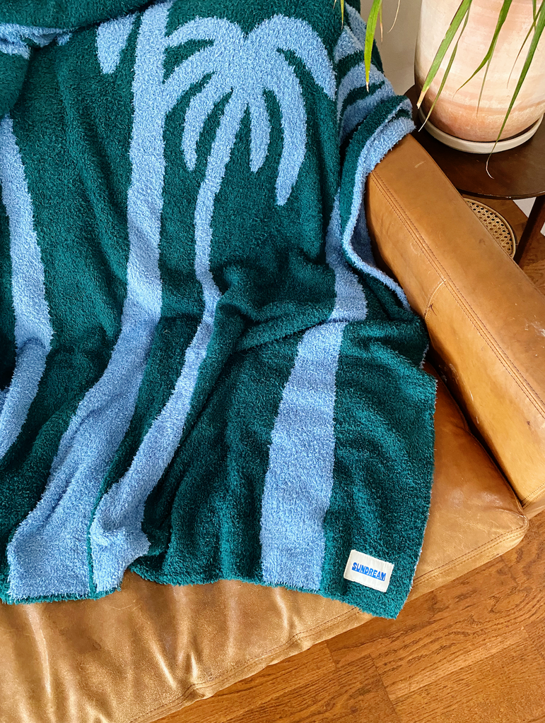 A teal and light blue throw blanket featuring a palm tree design, made of soft and plush material.