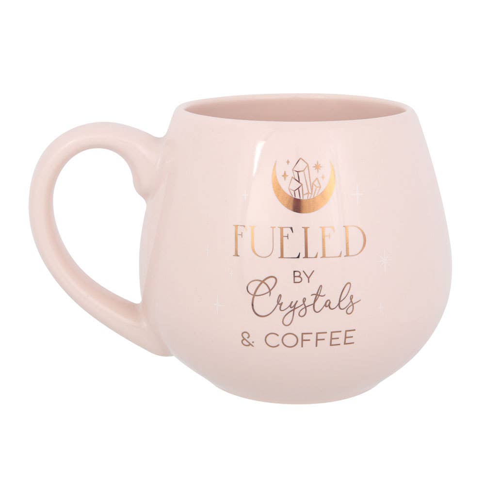 A stylish coffee mug with the text “Fueled by Crystals & Coffee,” surrounded by various crystals on a wooden table.