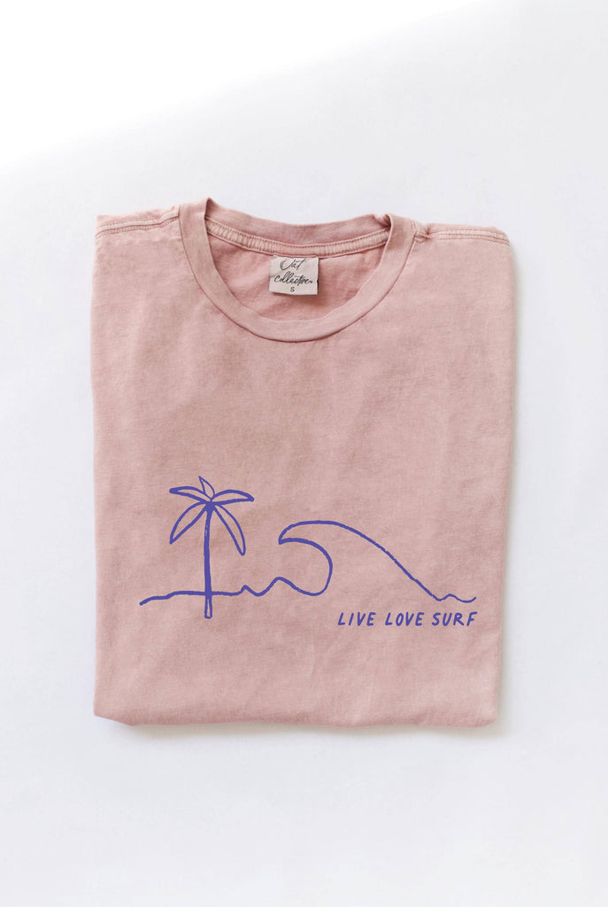 Folded soft pink-colored t-shirt with a blue minimalist palm tree, wave, and "LIVE LOVE SURF" graphic.
