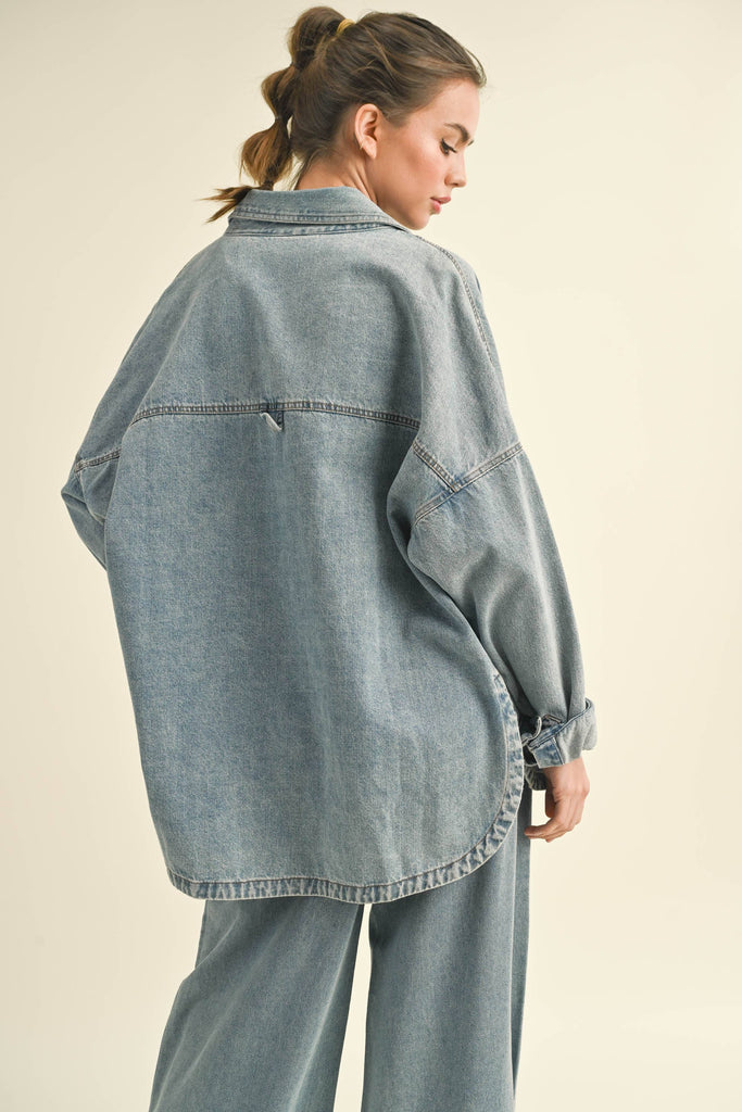 Model in an oversized denim jacket with front pockets. First image: jacket buttoned, paired with white shorts. Second image: jacket open, over a grey tank and denim pants.