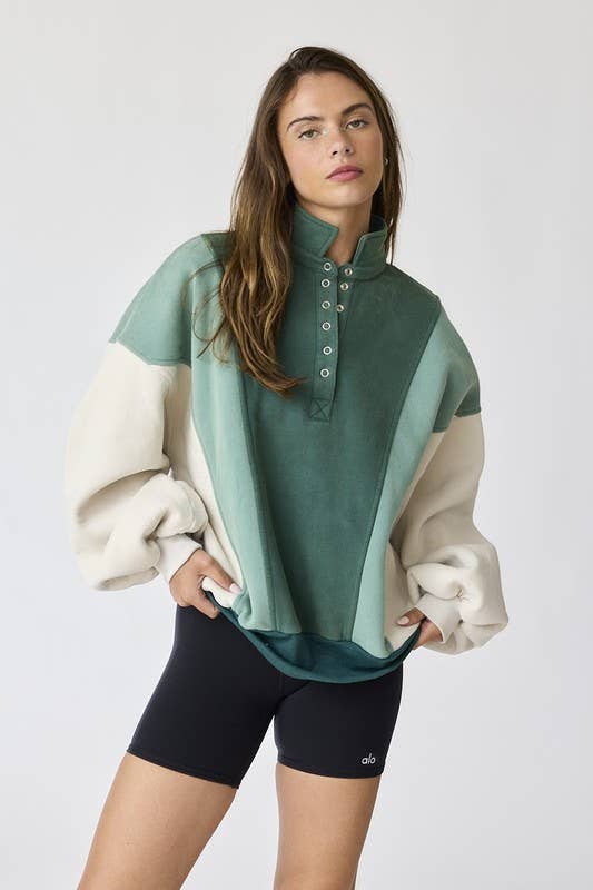 Woman wearing an oversized washed colorblock sweater in green and cream with black shorts.