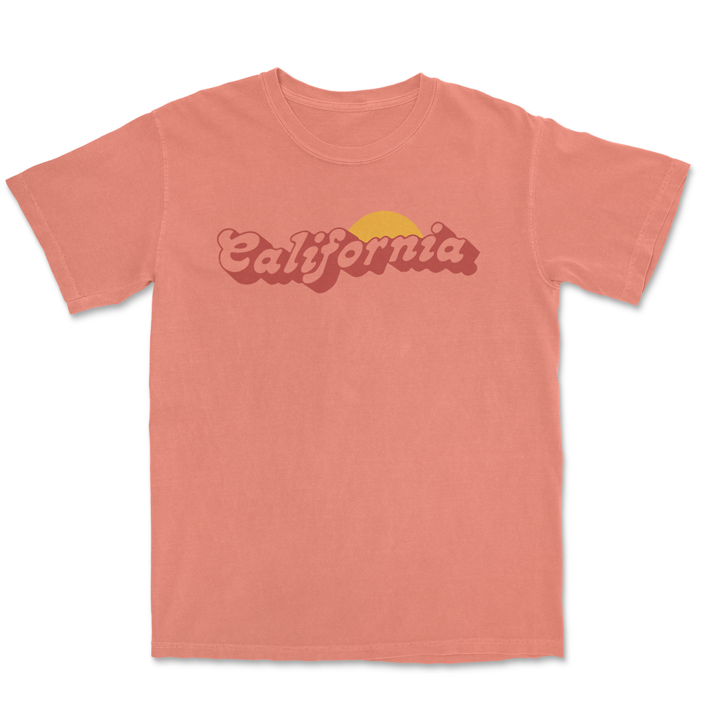 Vintage-inspired pink California T-shirt with a sun graphic on a sandy background.