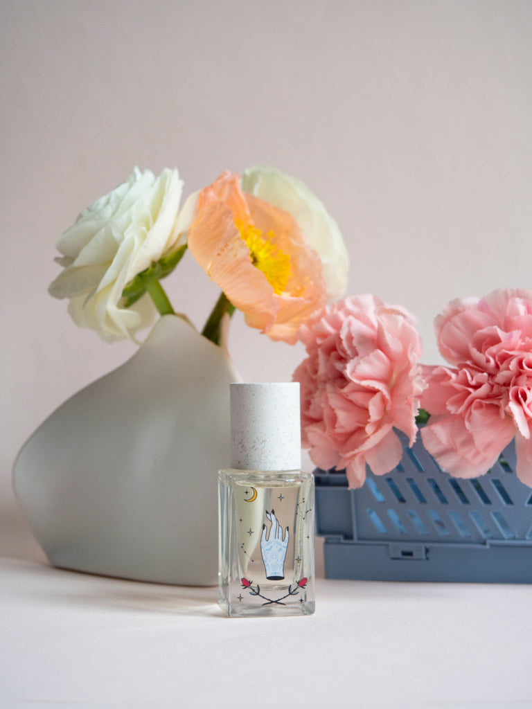 Maison Matine Avant l’Orage perfume bottle with celestial illustrations, placed among citrus fruits and sample vials on blue fabric