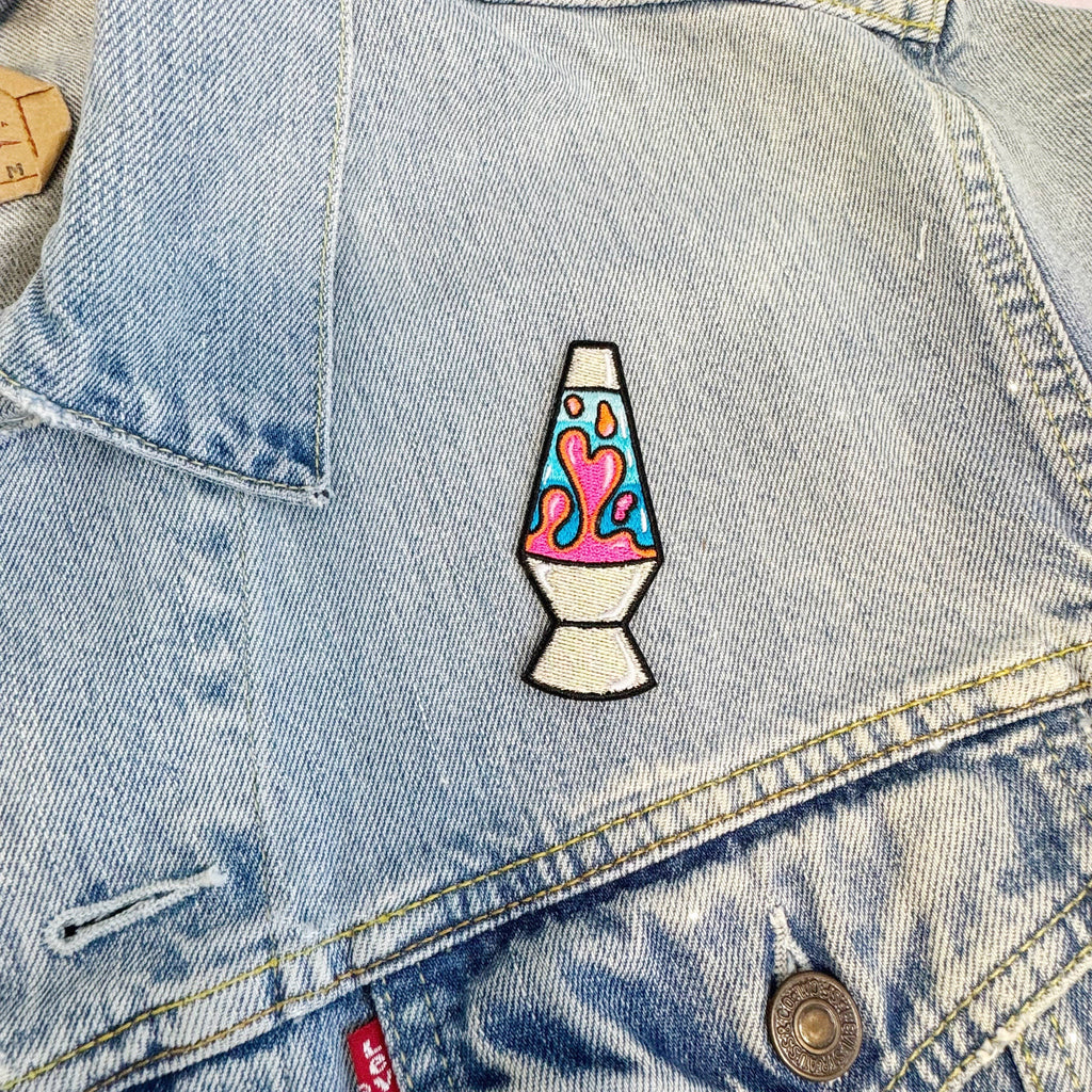 Colorful embroidered lava lamp patch on a pink fuzzy background.