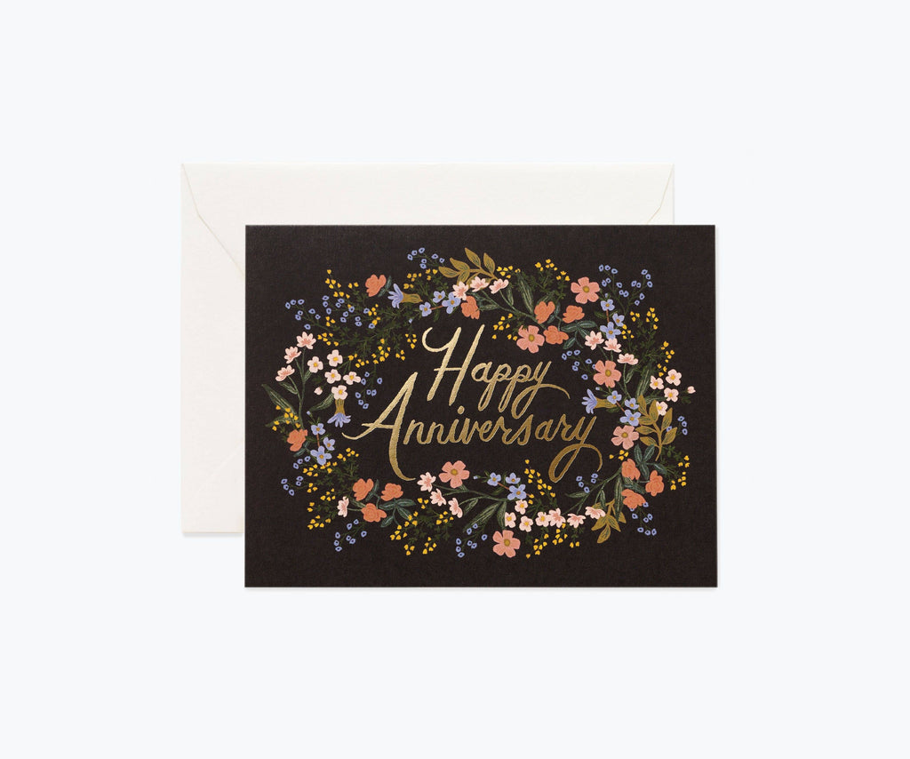 "Happy Anniversary" card with gold foil lettering surrounded by a floral wreath design on a black background, paired with a white envelope.