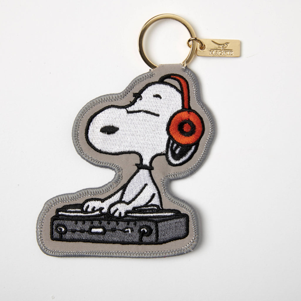 Embroidered keychain featuring Snoopy as a DJ, wearing headphones and standing at a DJ deck, attached to a gold-tone keyring.