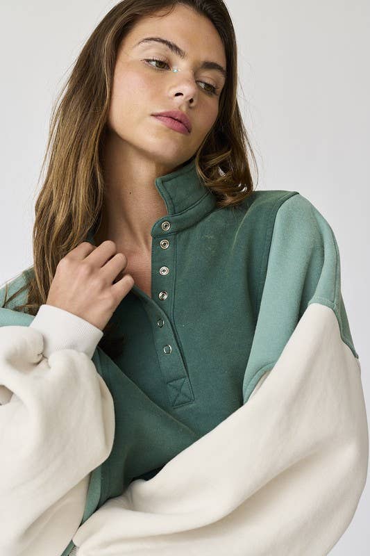 Woman wearing an oversized washed colorblock sweater in green and cream with black shorts.