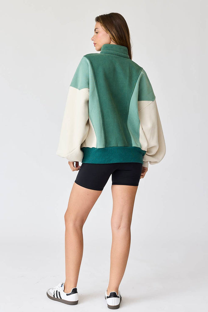 Woman wearing an oversized washed colorblock sweater in green and cream with black shorts.