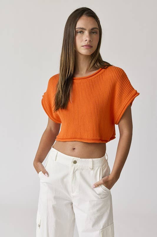 Woman wearing an orange cropped rib knit top with white pants.