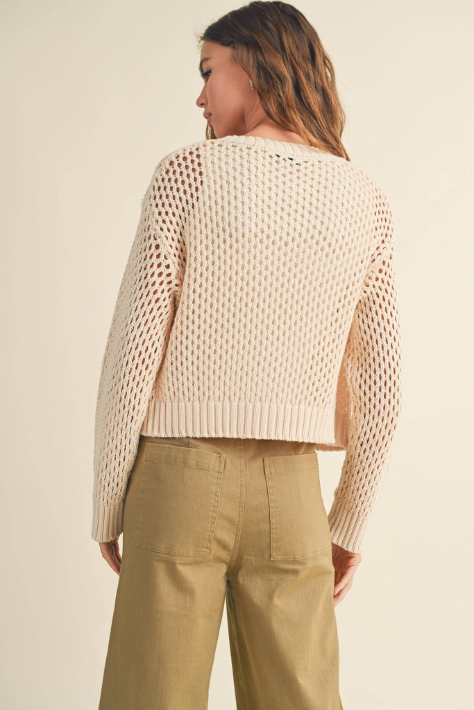 Model in a cream open-knit cardigan. cardigan over a white top and khaki pants. cardigan slightly open, paired with the same outfit.