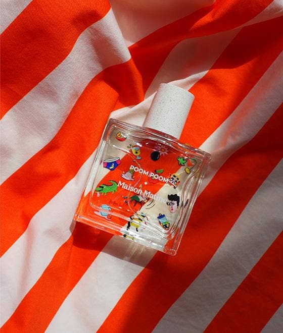 Poom Poom Eau de Parfum bottle with playful illustrations, displayed on an orange and white striped fabric background.