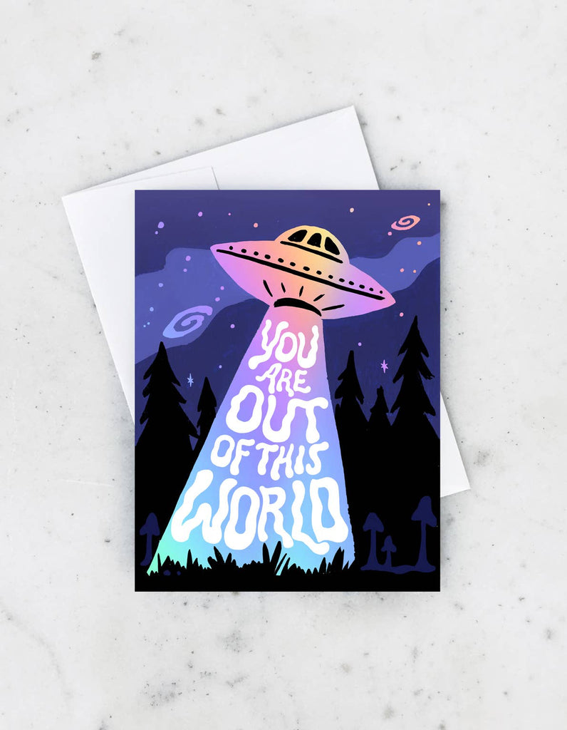 A greeting card with a vibrant design of a UFO beaming the words “You Are Out of This World” against a nighttime forest backdrop.