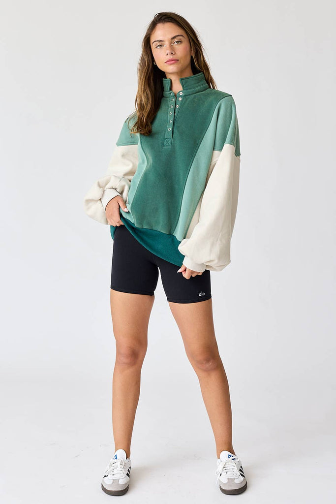 Woman wearing an oversized washed colorblock sweater in green and cream with black shorts.