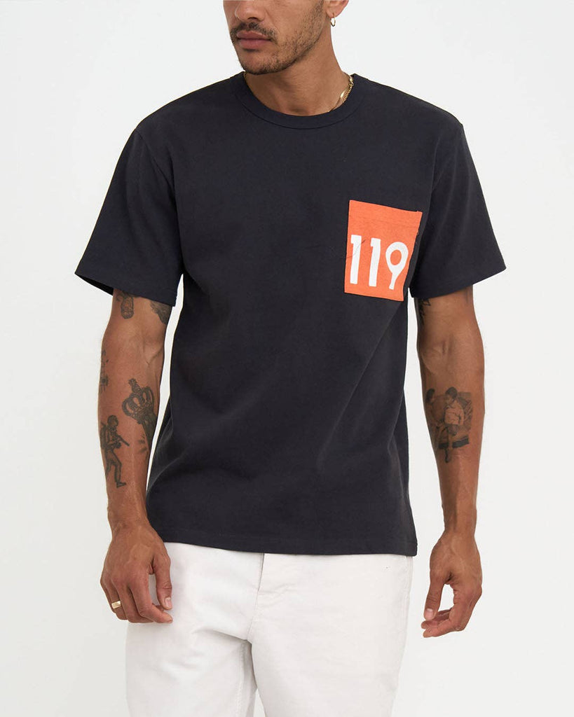 Front and back view of a man wearing a black t-shirt with a red-orange "119" pocket graphic and large "LA" text on the back, styled with white pants.