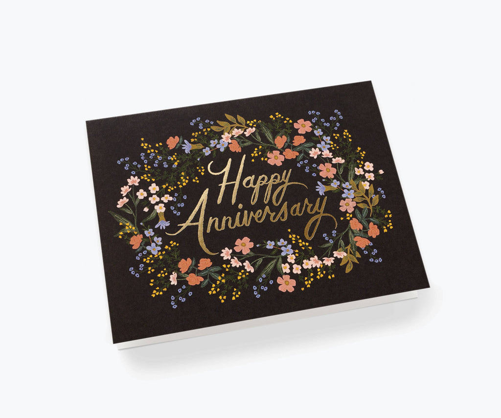 "Happy Anniversary" card with gold foil lettering surrounded by a floral wreath design on a black background, paired with a white envelope.