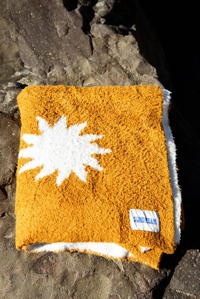 Cozy plush throw blanket in buckhorn brown with a white sunburst pattern, draped over a leather couch in a stylish and inviting living room.