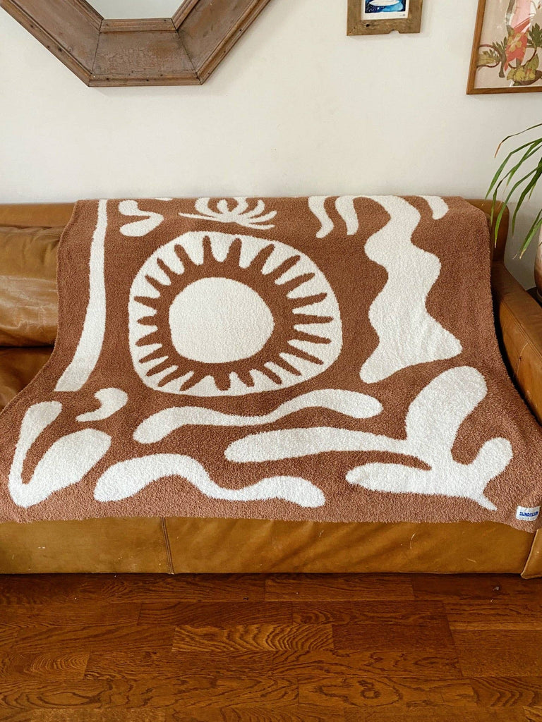 Soft brown plush throw blanket with a sun and palm tree design, perfect for adding warmth and a stylish accent to any space.