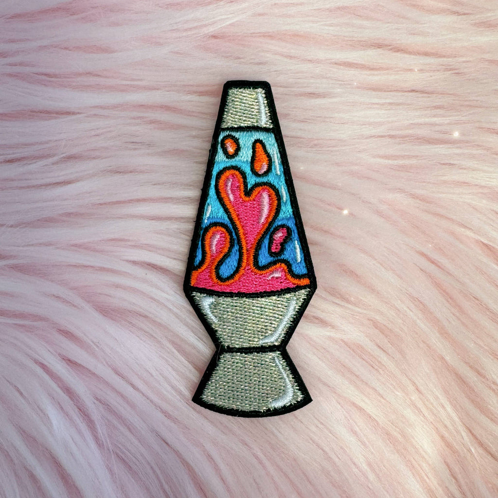 Colorful embroidered lava lamp patch on a pink fuzzy background.