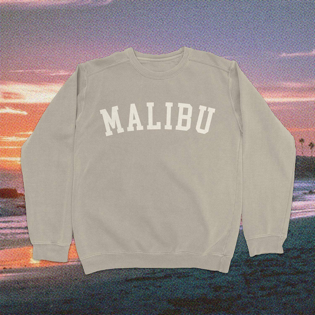 Neutral beige "Malibu" sweatshirt with white text set against a scenic Malibu sunset background.