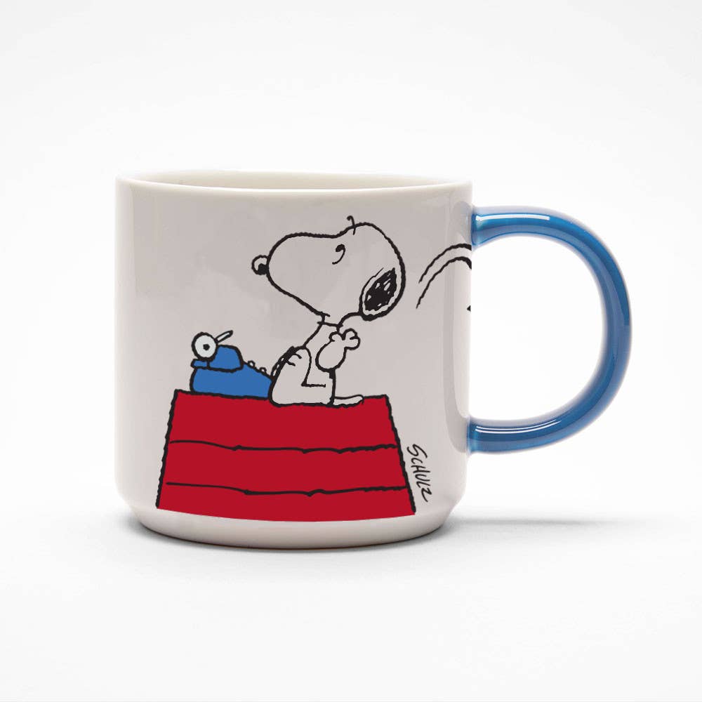 Ceramic mug featuring Snoopy sitting on a red doghouse with a typewriter, set against a white background with a blue handle.