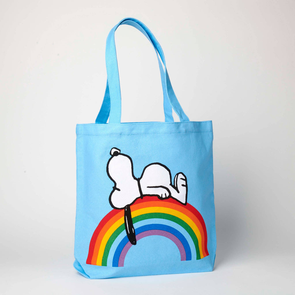 Blue tote bag featuring Snoopy lying on a colorful rainbow, ideal for fans of Peanuts and cheerful accessories.