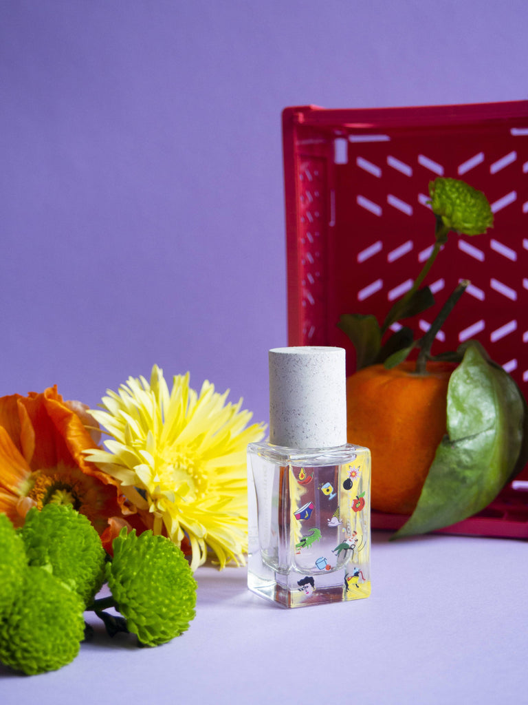 Maison Matine Poom Poom perfume bottle with playful illustrations, surrounded by colorful flowers and a tangerine