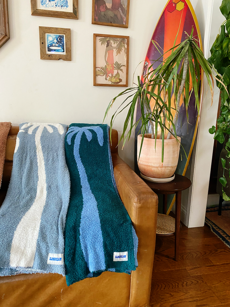 A teal and light blue throw blanket featuring a palm tree design, made of soft and plush material.