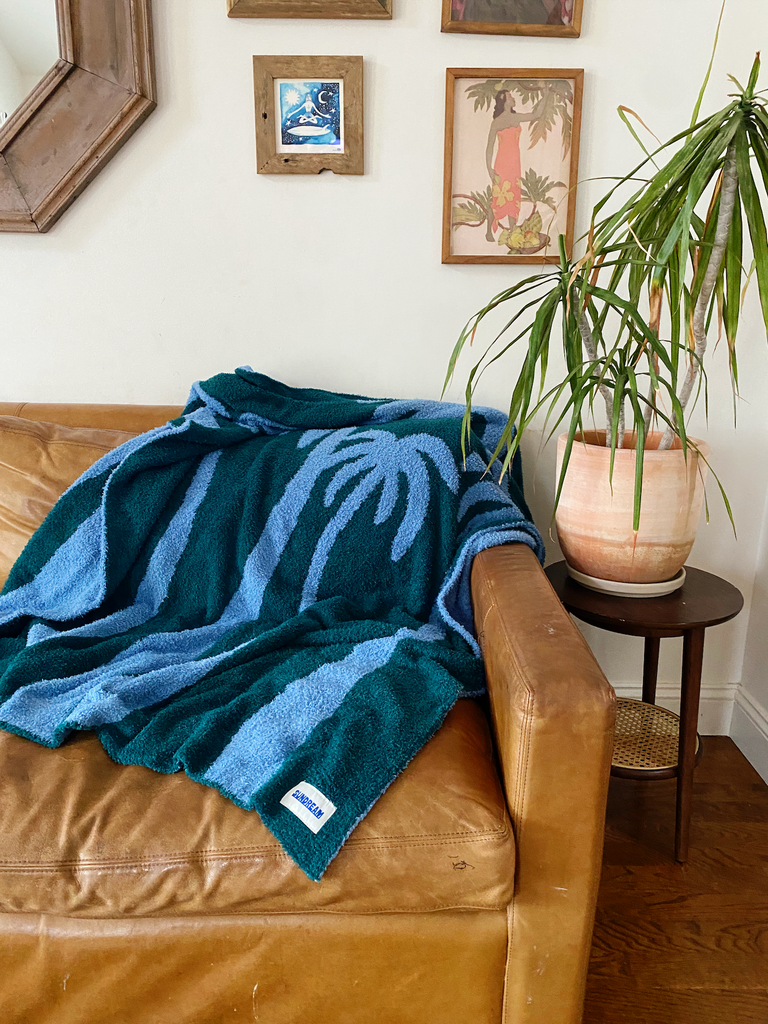 A teal and light blue throw blanket featuring a palm tree design, made of soft and plush material.