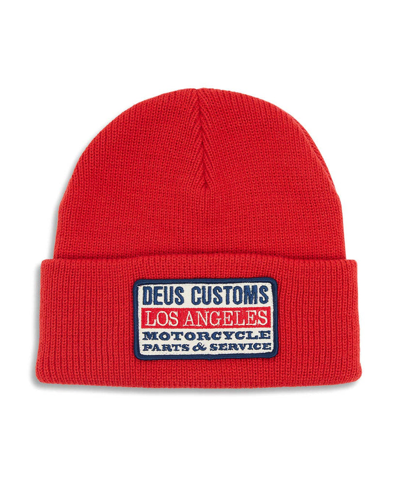 Red knit beanie with a rectangular patch that reads “DEUS Customs Los Angeles Motorcycle Parts & Service."