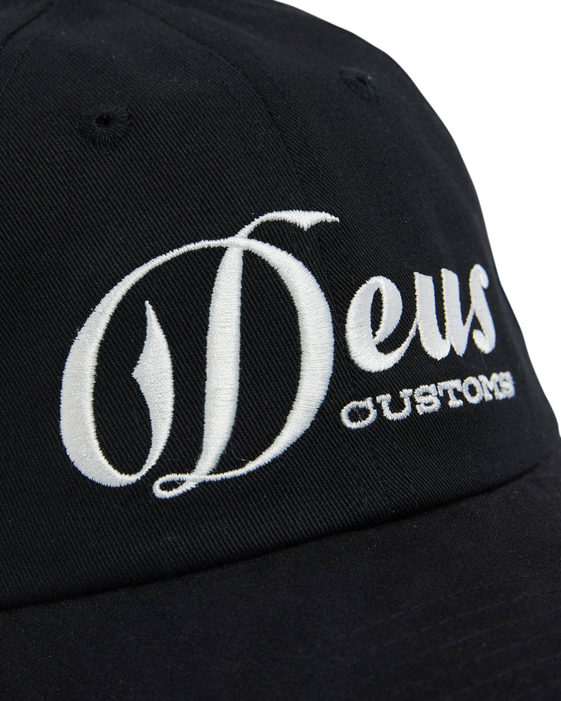 Black cap with white "Deus Customs" embroidery, curved brim, and adjustable fit.