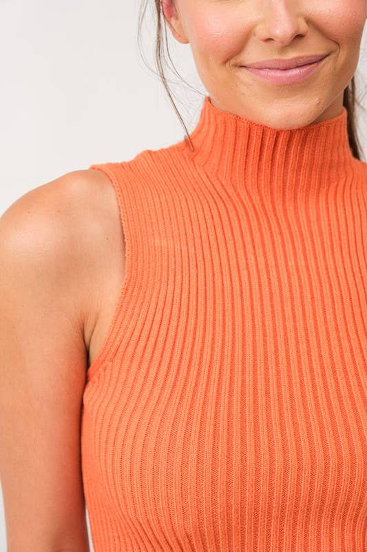 Woman wearing a cropped orange mock neck ribbed knit sweater.