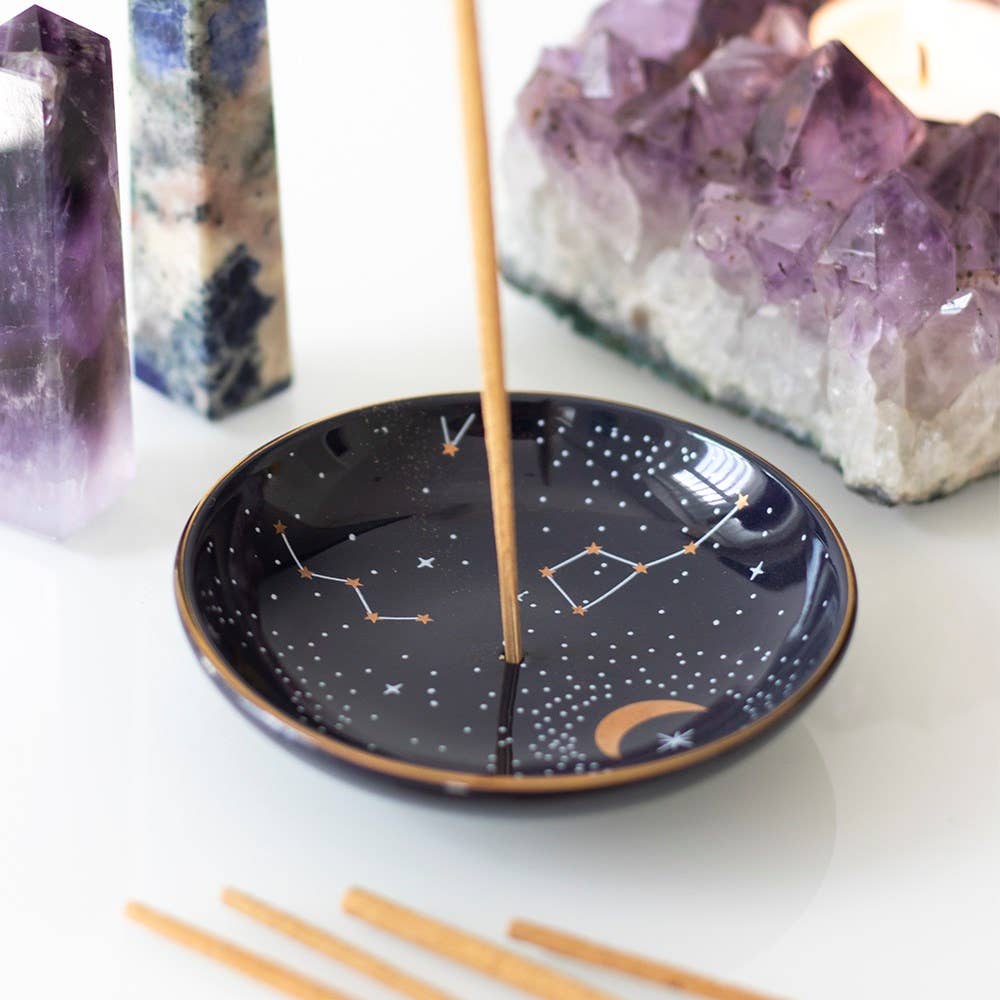 A celestial-themed ceramic dish with a constellation design, golden moons, and stars, used as an incense holder or jewelry tray.