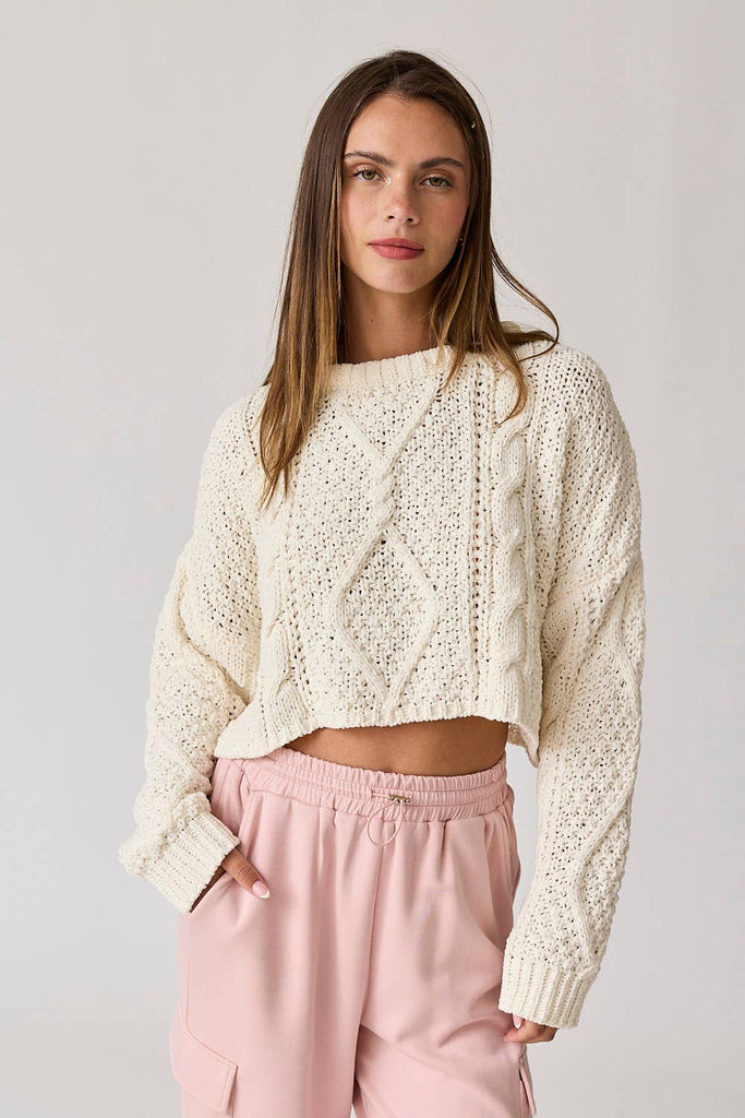 Woman wearing a loose-fit white cable knit sweater pullover with pink pants.