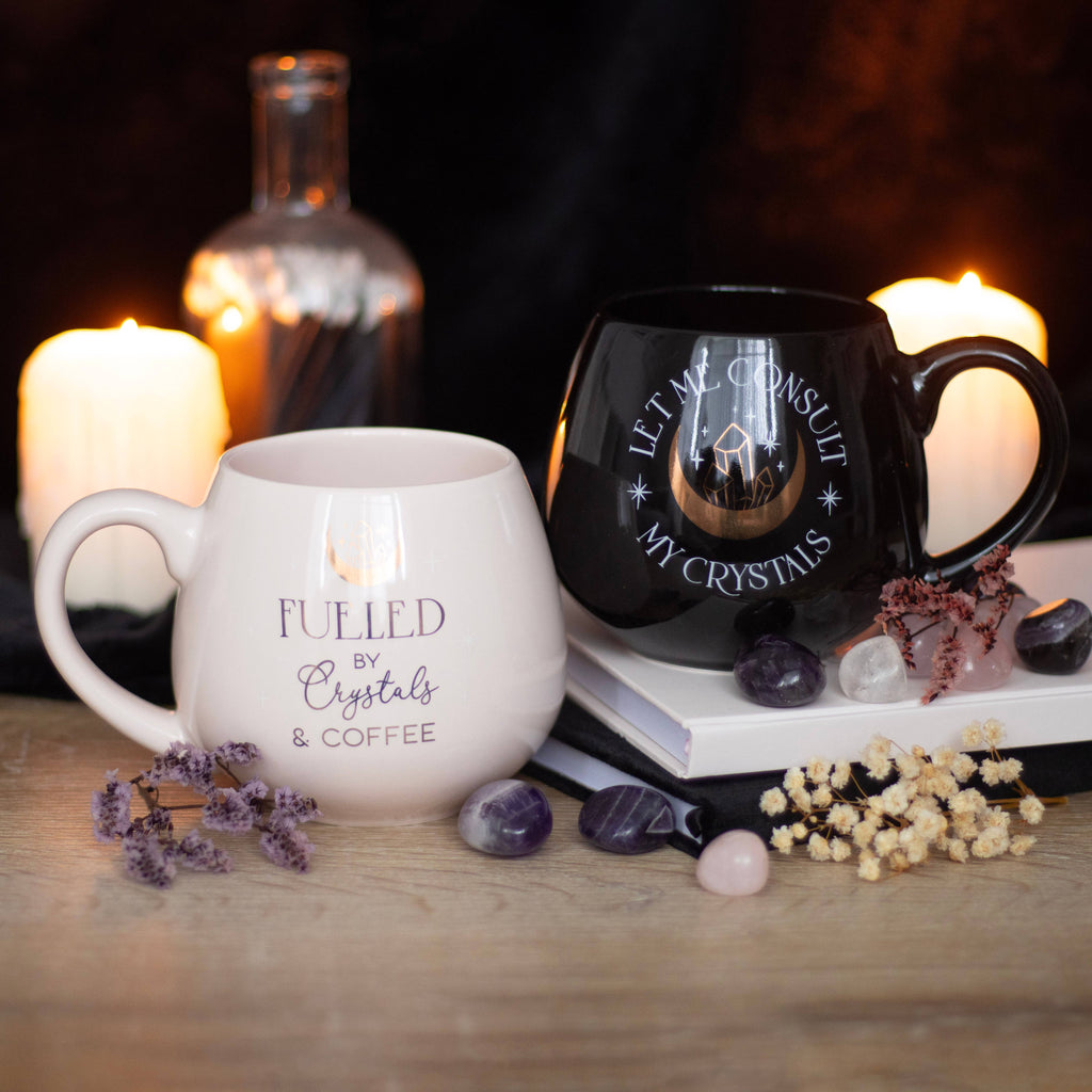 A stylish coffee mug with the text “Fueled by Crystals & Coffee,” surrounded by various crystals on a wooden table.