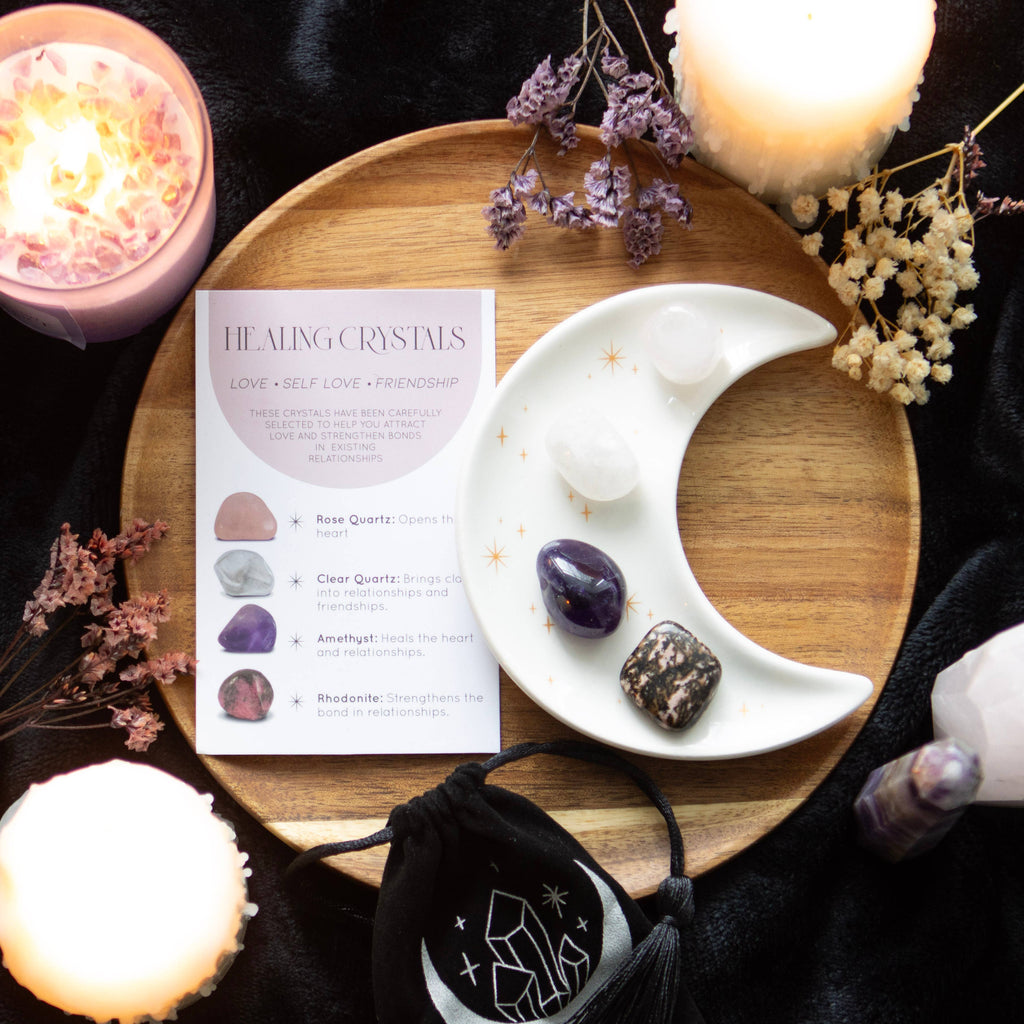 Love Crystal Set featuring a crescent moon trinket dish, rose quartz, clear quartz, amethyst, and rhodonite stones, displayed with a matching information card and a printed drawstring pouch.