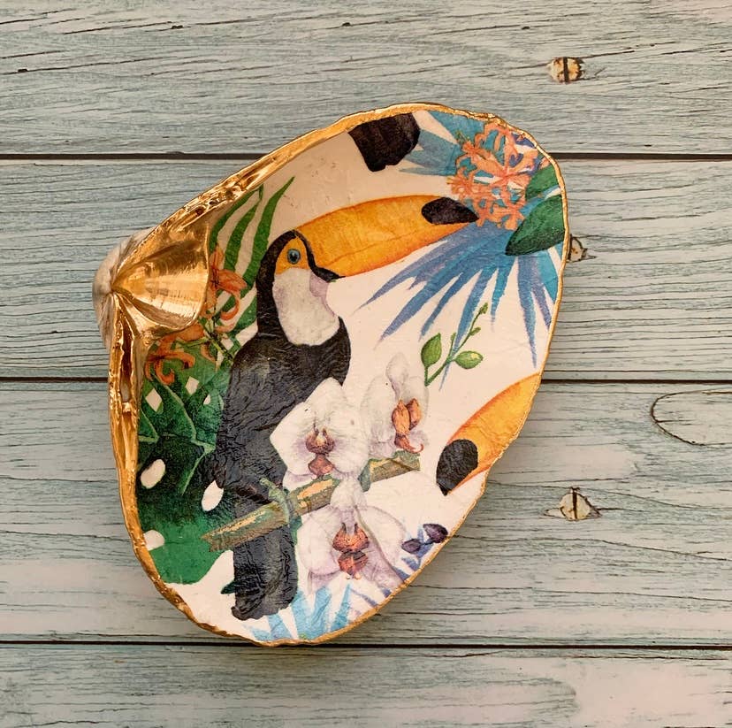 Decorative shell featuring a colorful toucan and tropical foliage with gold edges, ideal for adding a tropical flair to your home decor.